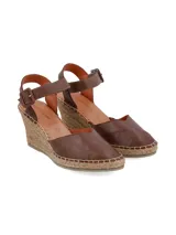 Sandalia de cuña Lora en cuero napa color marrón chocolate, con plataforma revestida en yute trenzado, puntera cerrada y tira ajustable al tobillo con hebilla forrada.