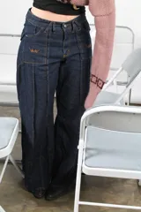 Pantalón jean azul oscuro de corte wide leg, con diseño holgado, bolsillos delanteros aplicados con detalles bordados y costuras verticales destacadas a lo largo de las piernas.