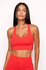 Top deportivo de alto rendimiento color rojo, con diseño de espalda nadadora y banda elástica inferior para mayor soporte. Cuenta con logo estampado en el frente y bolsillos integrados.