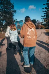 Canguro marrón con capucha y cordones ajustables. Presenta un estampado grande en la espalda con una ola, palmeras y el texto "Glassy Waves".