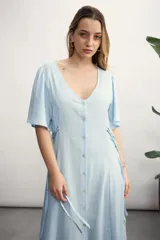 Vestido largo color beige claro, con escote en V, manga corta acampanada y cierre frontal de botones. Presenta un lazo ajustable en la cintura y un tejido con textura sutil.