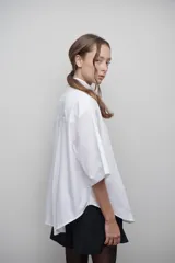 Camisa blanca de popelina 100% algodón, de diseño oversize y corte unisex. Presenta cuello clásico, manga amplia, bolsillo frontal y canesú con pliegue central en la espalda.