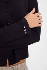 Blusa de algodón con cuello redondo, manga larga y cierre frontal con botones a tono. Presenta un diseño ajustado al cuerpo.