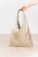 Bolso de hombro color beige, confeccionado en cuero sintético con interior plateado. Presenta un bolsillo externo con cierre.