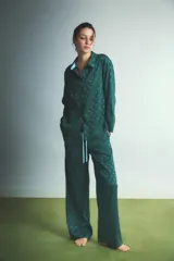 Pijama de dos piezas compuesto por camisa de manga larga con cuello camisero y botones frontales, y pantalón de corte recto y holgado con cintura elástica y cordón de ajuste. Presenta un diseño estampado con pequeños corazones en tono sobre tono.