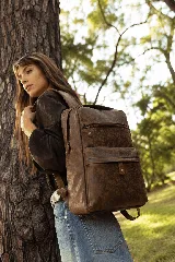 Mochila marrón de cuero genuino, con diseño estructurado, compartimento principal amplio apto para notebook, bolsillo frontal grande con solapa y cierre, bolsillo secundario con cierre y detalles metálicos.