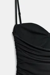 Vestido mini negro con escote corazón, aros en el busto y tirantes finos ajustables. Presenta un diseño drapeado en todo el cuerpo y un bajo con detalle de volante.