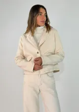 Chaqueta de pana color beige, de corte corto y diseño estructurado con cuello solapa, cierre frontal de un botón y bolsillos delanteros con solapa.