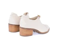 Zapato cerrado tipo mocasín con taco cuadrado de madera, confeccionado en cuero con textura de reptil en color crema. Presenta un detalle de hebilla metálica dorada en el empeine.