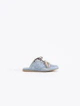 Zapatilla tipo mule (sin talón) de cuero vacuno, color celeste con efecto gastado y detalles de recortes. Presenta un logo estilizado en el lateral y cordones anchos de color beige y marrón.