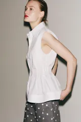 Camisa blanca de cuello solapa y sin mangas, con bajo acabado en peplum y cierre frontal con botones ocultos.