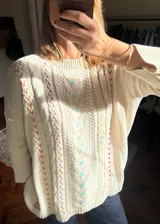 Sweater de hilo de algodón color beige, de diseño holgado con hombros caídos, tejido de ochos y detalles bordados a mano en varios colores.