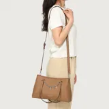 Cartera Guess modelo Angelica, color marrón símil cuero, con doble asa de hombro y correa regulable. Presenta un detalle de cadena metálica plateada con dijes colgantes que forman la palabra "GUESS" en la parte frontal, además del logo grabado en la base.