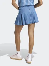 Minifalda plisada de denim azul, de talle medio, con diseño inspirado en la estética futbolística retro y cierre de cremallera.