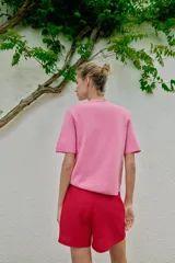 Chaqueta de punto de manga corta en color rosado, con cuello redondo y cierre frontal de botones dorados.