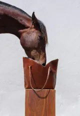Cartera de cuero color marrón chocolate con manijas largas y borde superior en corte en V. Diseño amplio y liviano, con terminaciones artesanales y costuras contrastantes en todo el contorno.