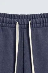 Pantalón jogger de corte wide fit confeccionado en algodón con interior de rizo. Presenta cintura elástica ajustable con cordón, bolsillos laterales y un bolsillo trasero de plastrón. Cuenta con un efecto lavado y acabados irregulares en el ruedo.