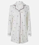 Camisón estilo americano de corte recto, confeccionado en viscolycra color blanco con estampado de pequeñas flores oscuras. Presenta cuello clásico, cierre frontal con botones, mangas largas con puños y detalles de biés en contraste.