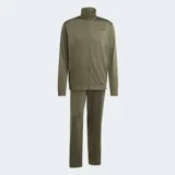 Conjunto deportivo Adidas compuesto por campera con cierre frontal y pantalón largo, ambos en color verde oliva. La campera presenta cuello alto y el pantalón cuenta con cintura elástica ajustable. Ambos incluyen bolsillos laterales y el logo de la marca estampado en tono oscuro.