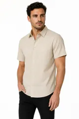 Camisa de manga corta color beige con sutiles rayas verticales, cuello camisero, cierre frontal con botones y un bolsillo aplicado en el pecho.
