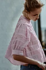 Camisa rosa de cuello alto, mangas cortas abullonadas y detalles de encaje y entredós en el frente y las mangas.