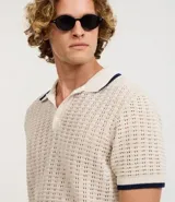Camisa polo de manga corta, color beige claro, con textura de tejido abierto tipo ganchillo. Posee cuello y ribetes en las mangas en color azul marino.