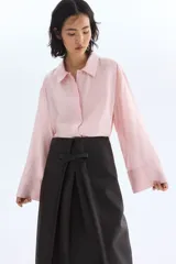 Camisa oversize de manga larga en mezcla de viscosa, color rosado claro. Cuenta con cuello camisero clásico, cierre frontal con botonadura oculta y canesú en la espalda. Presenta hombros caídos, puños anchos y bajo recto con aberturas laterales.