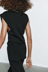 Top de algodón color beige con cuello recto, mangas asimétricas y detalle de tejido drapeado en el frente.