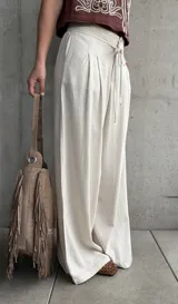 Pantalón palazo de lino color beige, de calce amplio y fluido, con tablas en el frente, botón, cierre y cordón ajustable en la cintura.