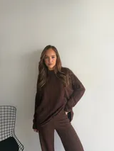 Buzo de punto color marrón chocolate, con cuello redondo y diseño holgado de manga larga con textura de trenzas verticales.