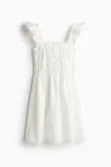 Vestido corto blanco de algodón con broderie, escote recto, breteles anchos con volados fruncidos y cuerpo entallado con frunces elásticos.