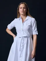 Vestido camisero blanco de algodón con cuello con solapa, delantera abotonada, mangas 3/4 regulables con presilla y botón, y cintura con lazo de ajuste.