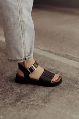 Sandalia de cuero color tostado con tiras anchas, tira en el talón y hebilla metálica rectangular ajustable. Cuenta con suela de goma con tacón bajo y plataforma.