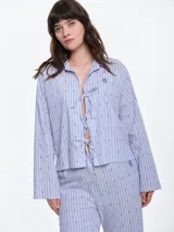 Camisa de dormir de popelina de algodón, con estampado de rayas verticales y pequeños motivos geométricos. Presenta cuello camisero, mangas largas y cierre frontal mediante lazos ajustables.
