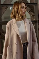 Tapado de paño color rosado, de corte oversized y diseño cruzado. Presenta solapas clásicas, mangas largas con puños vueltos y amplios bolsillos delanteros. Cierre frontal con un botón visible.