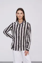Camisa de manga larga con cuello clásico y cierre frontal de botones. Presenta un estampado de rayas verticales irregulares en tonos oscuros, blancos y verde claro.