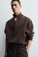 Jersey de punto de corte regular, color gris oscuro, con cuello subido y cierre frontal de cremallera. Presenta mangas largas y acabados en rib en puños y ruedo.
