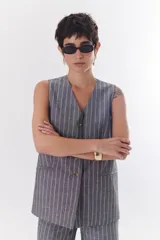 Chaleco largo color blanco con rayas verticales finas color beige, con cuello en V y cierre frontal con botones marrones. Incluye pañuelo al cuello con estampado de lunares y rayas.