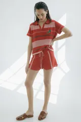 Short tejido en jersey color crudo con cintura elastizada azul marino y cordón de ajuste naranja. Presenta rayas verticales en los laterales con detalles de punto y terminaciones desflecadas.