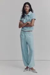 Saco corto de manga corta color celeste confeccionado en sherpa suave. Presenta cuello camisero, cierre frontal de botones metálicos dorados, bolsillos de parche en el pecho con solapa y botones, y diseño de bajo recto.