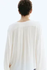 Blusa oversized de viscosa color beige con escote en V pronunciado, cordones ajustables con cuentas en los extremos, hombros caídos y mangas globo largas con puños elásticos.