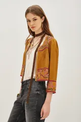 Chaqueta corta color mostaza con mangas abullonadas y bordados étnicos en tonos rosados y rojos en el frente, puños y hombros. Presenta un cierre frontal con detalles de cuentas.