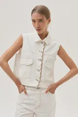 Chaleco de denim blanco con costuras en contraste color ocre, cuello camisero, cierre frontal con botones, bolsillos de parche con solapa en el pecho y sisas desflecadas.