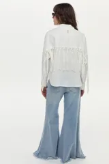 Camisa blanca de manga larga con flecos en la espalda y las mangas, confeccionada en mezcla de algodón, poliamida y elastano.