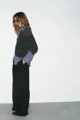 Pantalón de tiro medio con corte recto y holgado. Presenta pinzas en el delantero, trabillas para cinturón y cierre frontal con cremallera, botón y gancho metálico. Incluye bolsillos laterales y detalle de tapetas en la parte trasera.