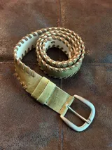 Cinturón de cuero color verde pistacho con detalles entrelazados en cuero gamuza color cocoa. Presenta hebilla metálica plateada y ojales reforzados.