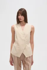 Chaleco color beige claro, sin mangas, con escote en V profundo y cierre frontal asimétrico con botones.