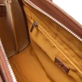 Cartera tipo tote de diseño estructurado en color habano, con textura granulada. Presenta doble asa superior, correa ajustable extraíble, cierre frontal con hebilla metálica decorativa y logo de la marca en la parte inferior.