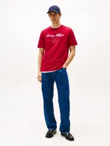 Remera de algodón de corte regular, color rojo, con cuello redondo y mangas cortas. Presenta el logotipo de la marca bordado en el pecho en tipografía cursiva y la bandera distintiva de Tommy Hilfiger bordada en la manga.
