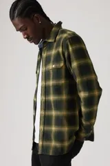 Camisa de manga larga a cuadros en tonos verde oscuro y amarillo, con cuello clásico, cierre de botones frontales y dos bolsillos con solapa en el pecho.